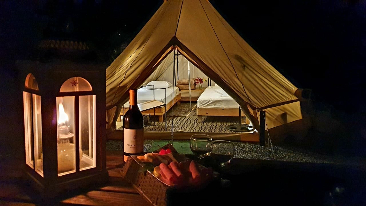 Interior de una tienda de glamping de noche, con dos camas hechas y un farol encendido