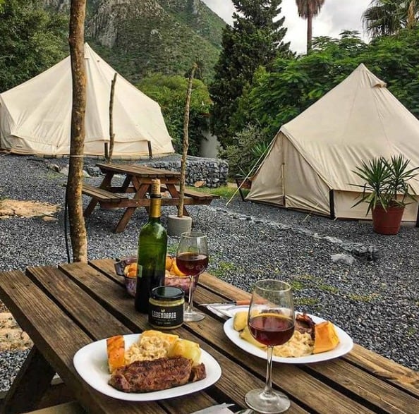Mesa servida frente a dos tiendas de glamping, con la montaña detrás