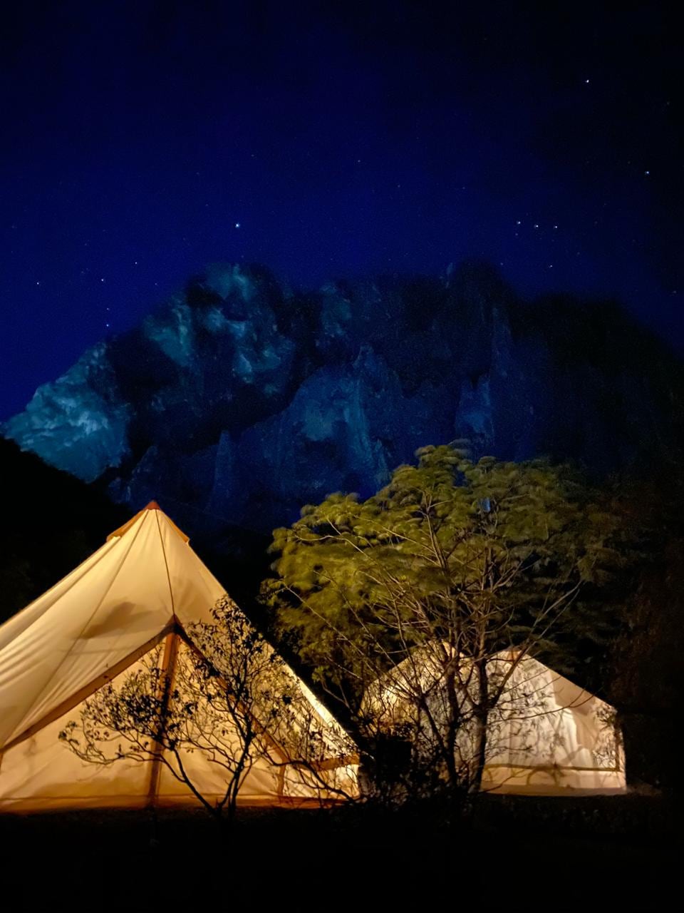 Dos tiendas de glamping iluminadas de noche, con la pared y las estrellas detrás